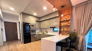 A modern kitchen with a central island, bar stools, wooden shelves with plants, and a view of the outdoors. - Luxury 3-bedroom apartment in Hulhumale,Maldives (Malé)