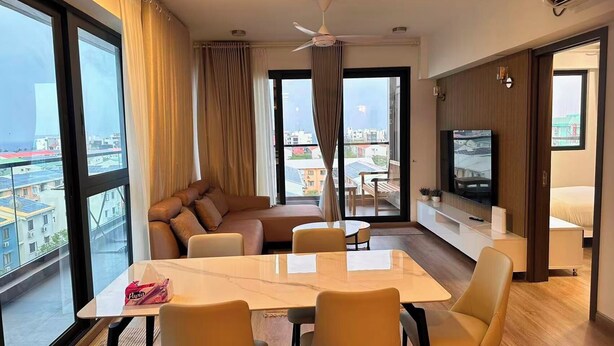 A modern hotel room with a large balcony, a dining area, a sofa, a TV, and a bed. - Luxury 3-bedroom apartment in Hulhumale,Maldives (Malé)
