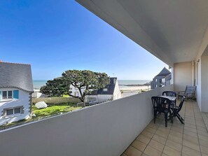 Ein Balkon mit Blick auf das Meer, einen Baum und einen Tisch mit Stühlen.