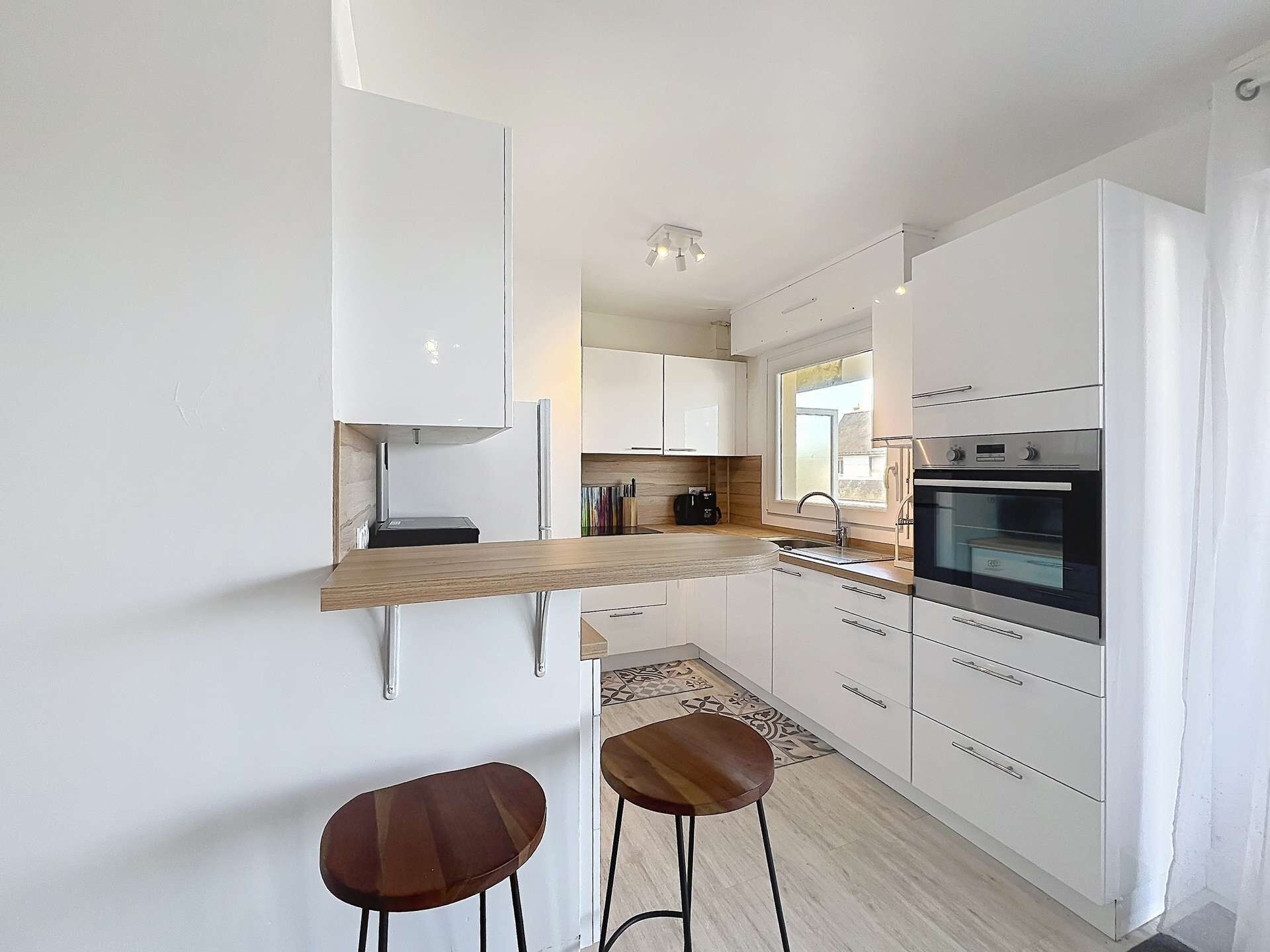 Eine moderne Küche mit weißen Schränken, einer Holz Arbeitsplatte, zwei Barhocker und einem eingebauten Ofen.