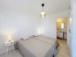Ein Schlafzimmer mit zwei Betten, einem Nachttisch mit Lampe, einer Pendelleuchte und einem durch eine offene Tür sichtbaren Badezimmer.