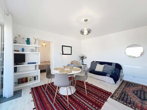 A modern living room with a dining area, white walls, a sofa, a TV, and a bookshelf. - Quiberon - 2 rooms - 43m² - WIFI (QUIBERON)