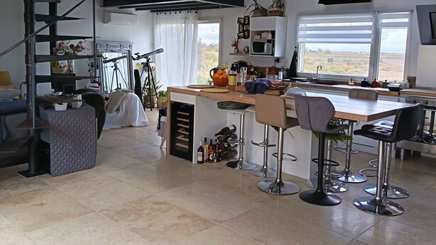 A spacious kitchen with a high ceiling, a built-in island with bar stools, a large window with a view, and a staircase leading to an upper level. - Lotf au stes maries de la mer (Saintes-Maries-de-la-Mer)