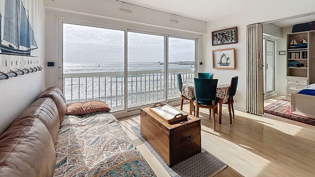 Un vaste espace de vie avec une grande porte-fenêtre coulissante donnant sur un balcon offrant une vue sur la mer.