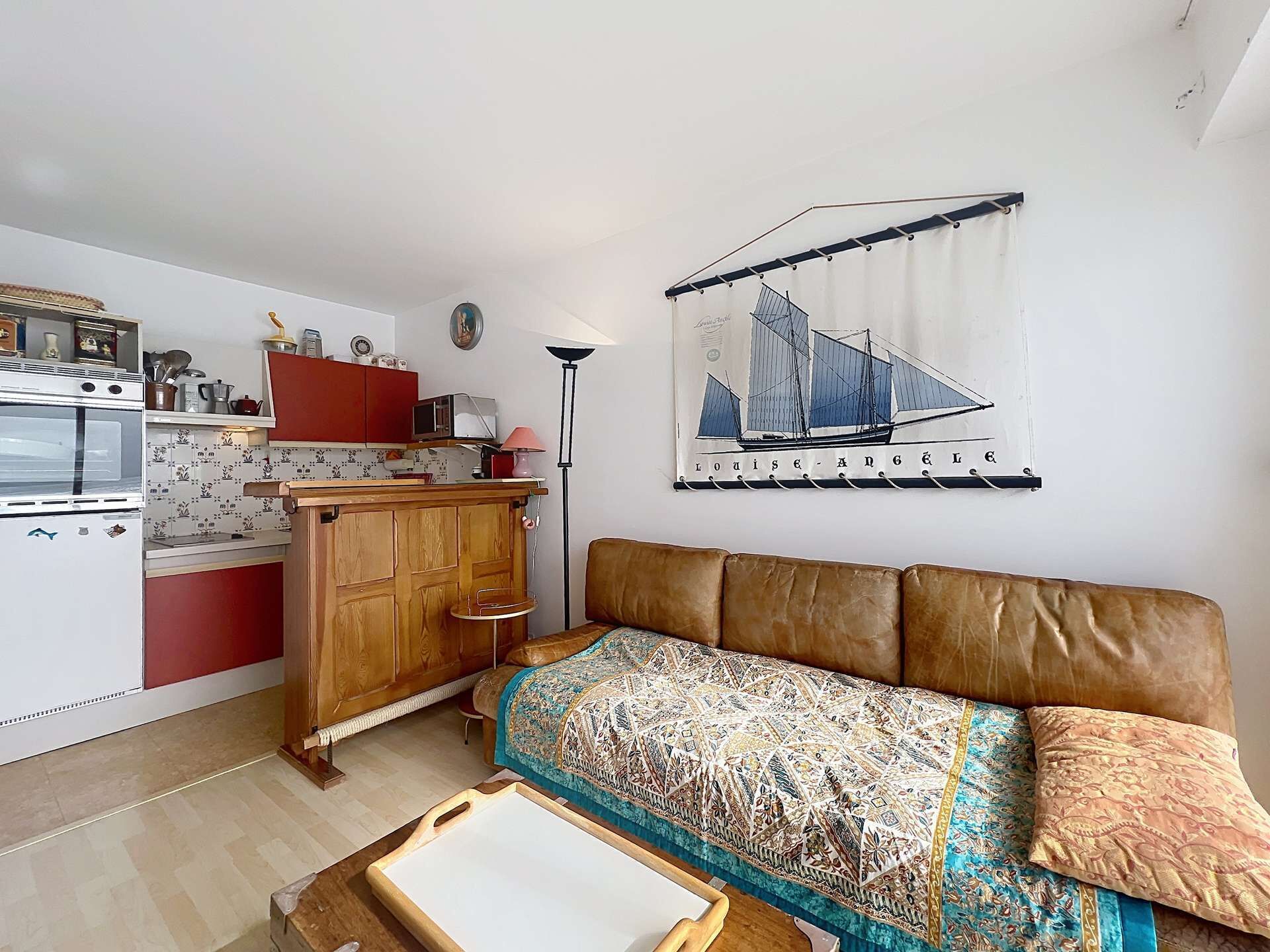 A compact living space with a kitchenette, a sofa, a patterned throw, and a sailboat painting.