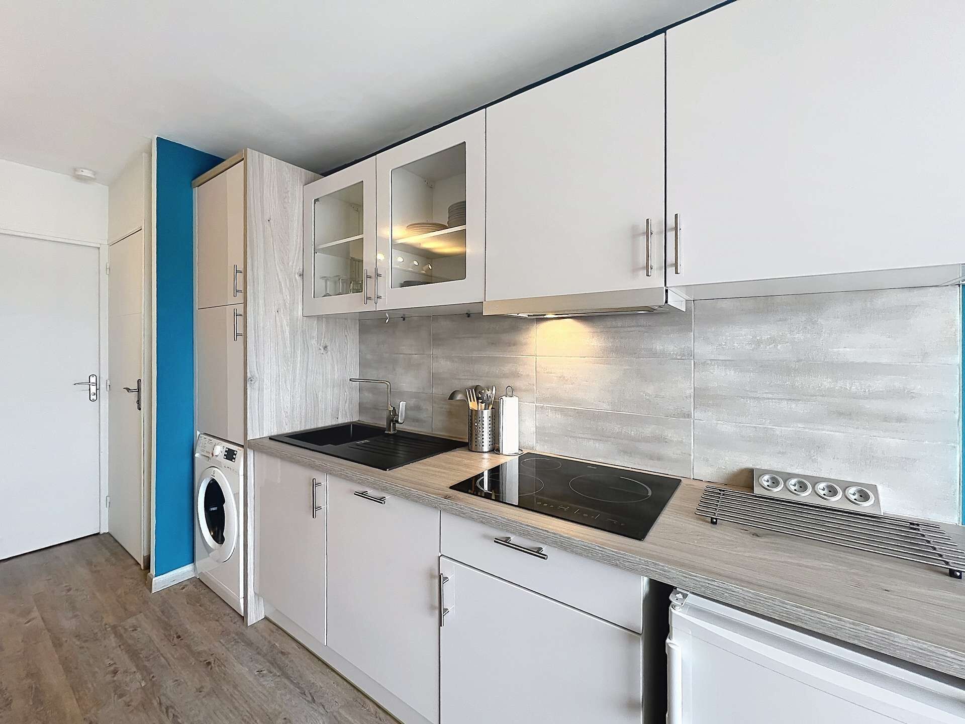 A compact kitchen with a washing machine, a stove, and cabinets.