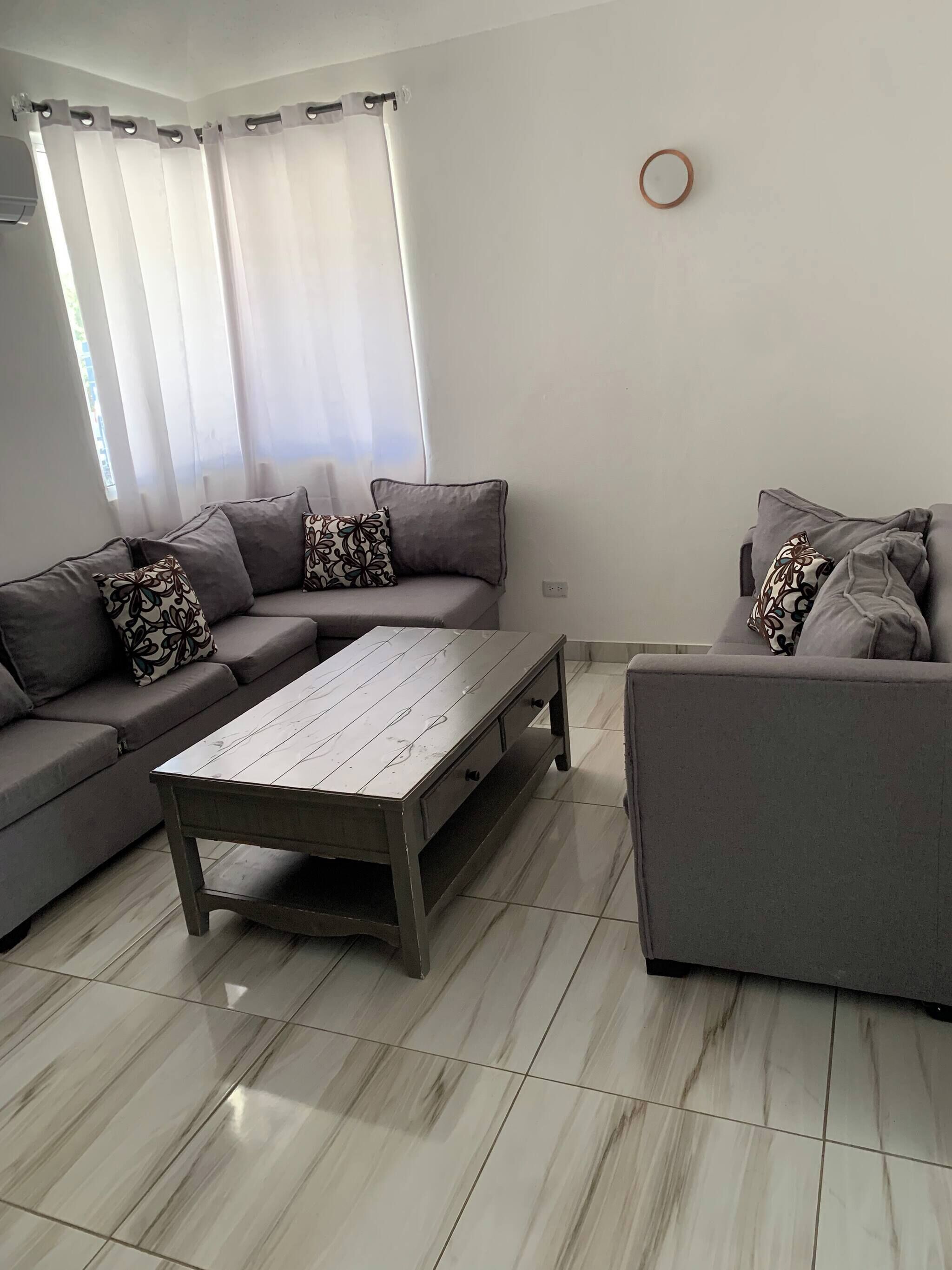 A modern living room with a grey sofa set, a wooden coffee table, and a tiled floor.
