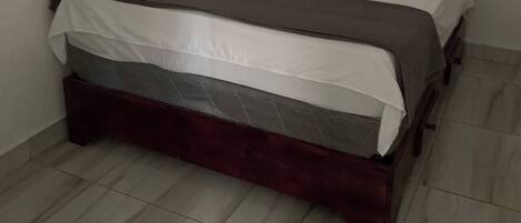 A small, neatly made bed in a corner room with white walls and a tiled floor.