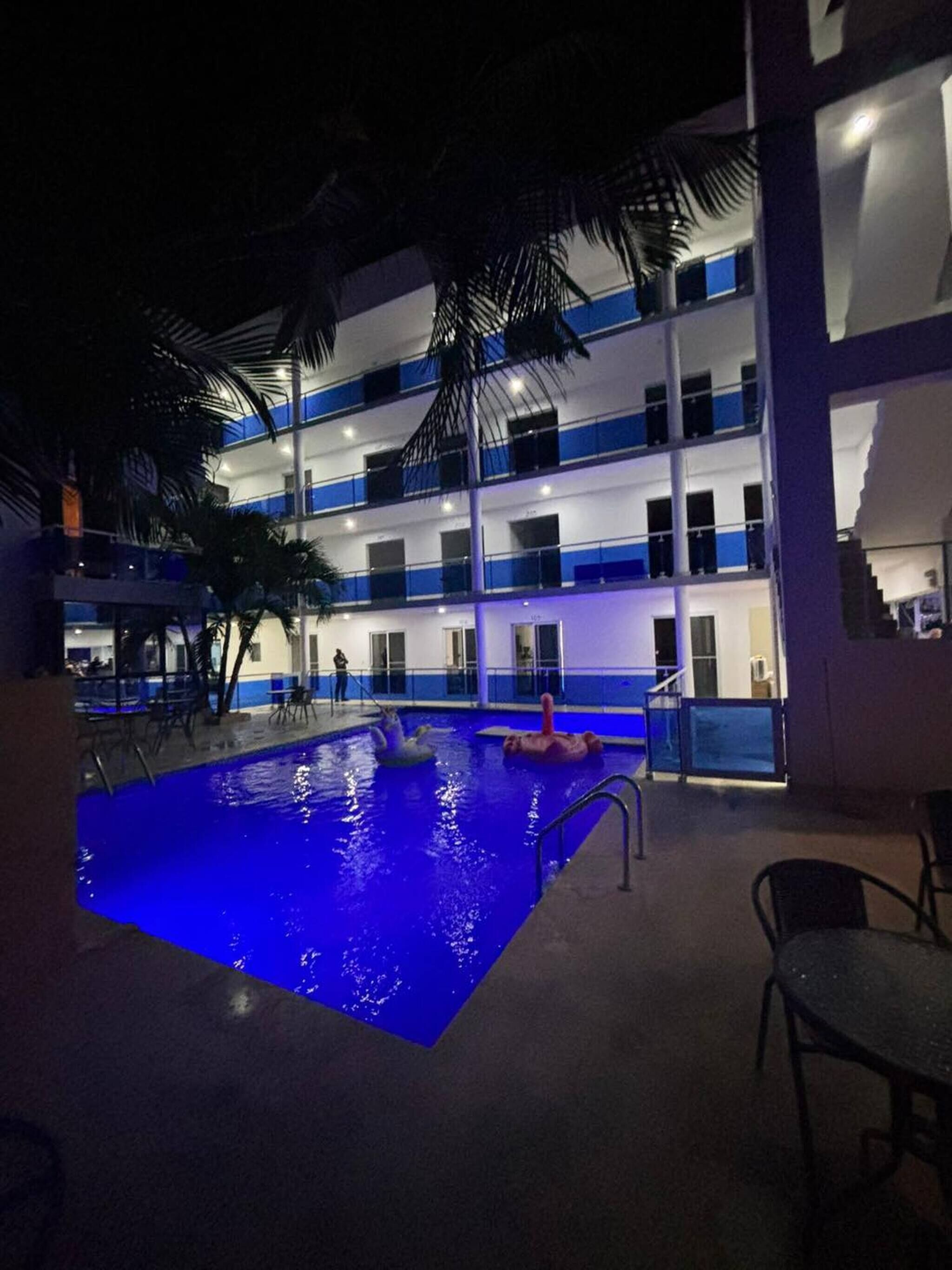 A multi-story hotel with a swimming pool, palm trees, and outdoor seating.
