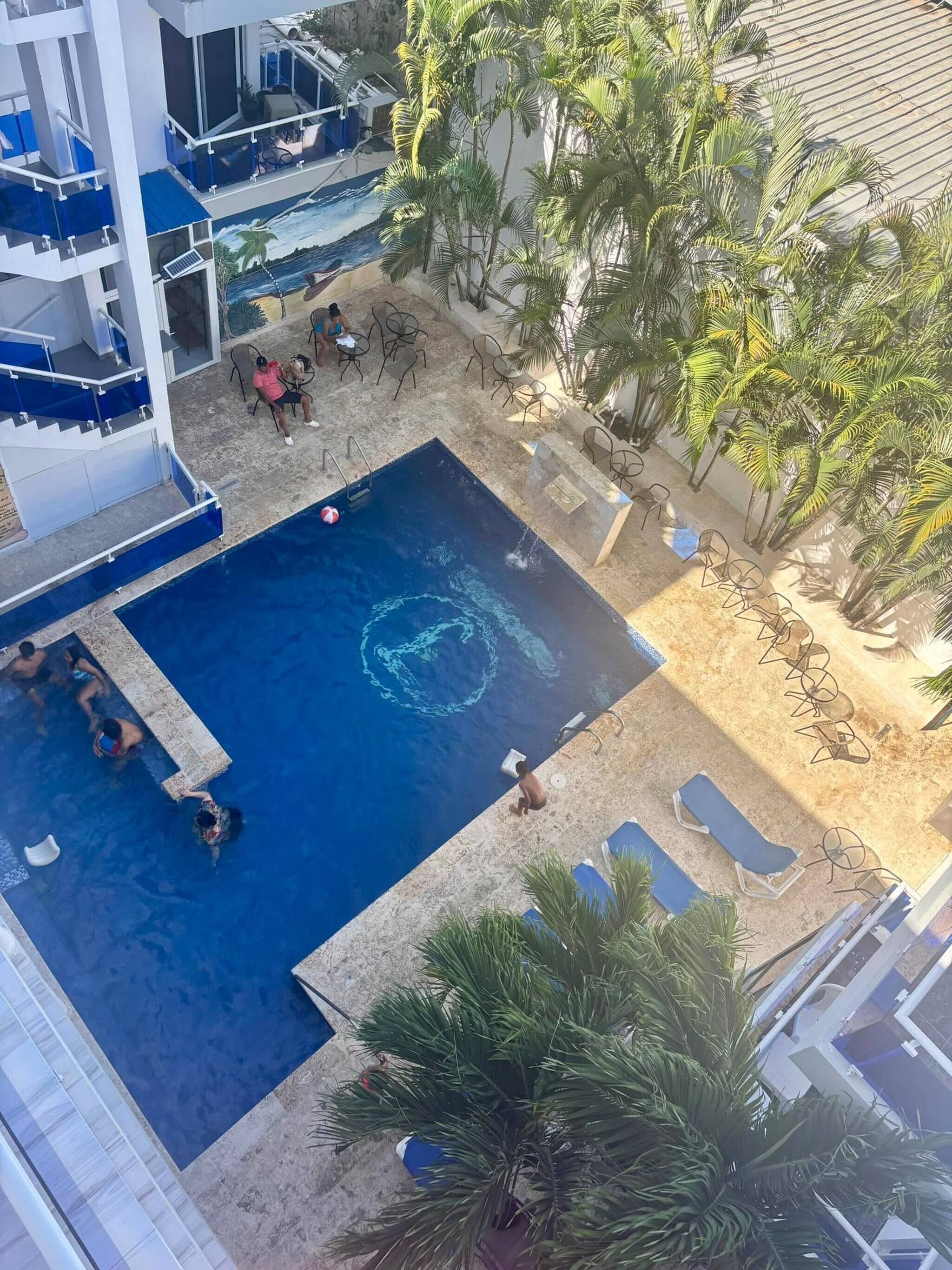 A pool area with lounge chairs, a diving board, and palm trees.