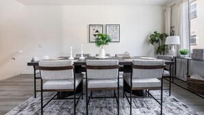 A dining area with a rectangular table, four grey upholstered chairs, a patterned rug, and two wall-mounted light fixtures. - Cozy Stay Near San Diego With 2 Car Garage (Lemon Grove)