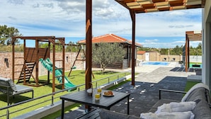 Um alpendre coberto com piscina, área de estar ao ar livre e espaço de recreação infantil.