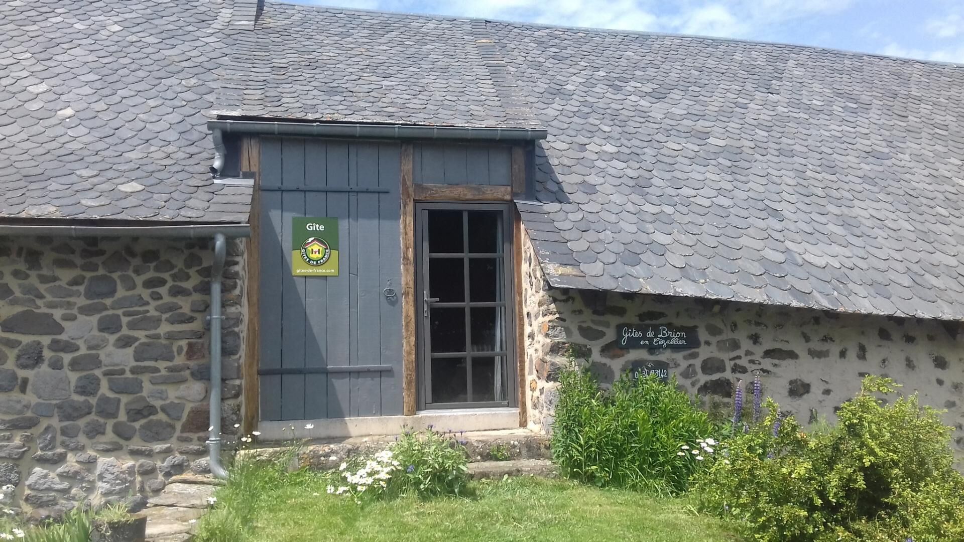 A stone building with a slate roof, a wooden door, and a sign indicating it's a gîte.
