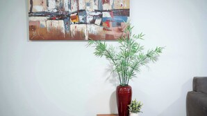 A room with a large abstract painting on the wall, a red vase with green plants on a wooden table, and a gray sofa. - Brilliant Apartment on Brisbane - Walk Everywhere! (Dubbo)