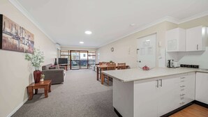 A modern kitchen with white cabinets, a central island, and a dining area with a table and chairs. - Brilliant Apartment on Brisbane - Walk Everywhere! (Dubbo)
