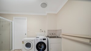 A laundry room with a front-loading washer and dryer, a sink, and a tiled floor. - Brilliant Apartment on Brisbane - Walk Everywhere! (Dubbo)