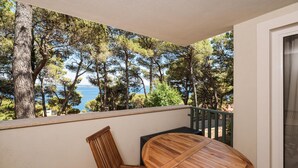 A balcony with a round wooden table and two chairs, overlooking a scenic view of trees and a body of water. - Cozy apartment in Kukljica with WiFi (Kukljica)