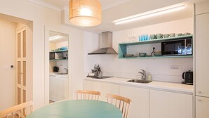 A modern kitchen with white cabinets, a teal dining table, and a hanging light fixture. - Cozy apartment in Kukljica with WiFi (Kukljica)