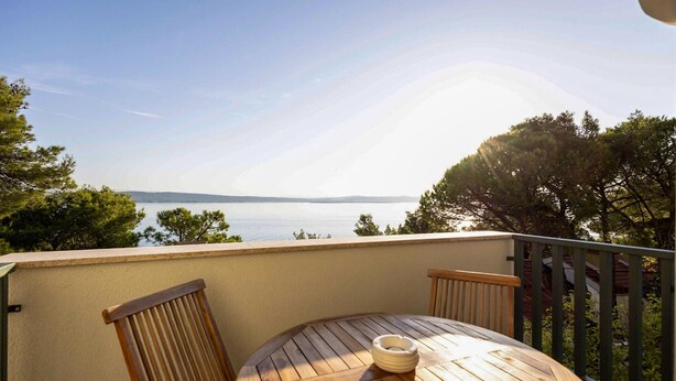 A round wooden table with a white object on it, two wooden chairs, and a view of the sea and mountains in the background. - Lovely apartment in Kukljica with house sea view (Kukljica)