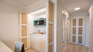 A compact kitchen with white cabinets, a microwave, and a sink. There are wicker doors and a small countertop with kitchenware. - Lovely apartment in Kukljica with house sea view (Kukljica)