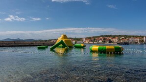 A waterfront area with inflatable water toys and a clear view of a coastal town with buildings and mountains in the background. - Lovely apartment in Kukljica with house sea view (Kukljica)