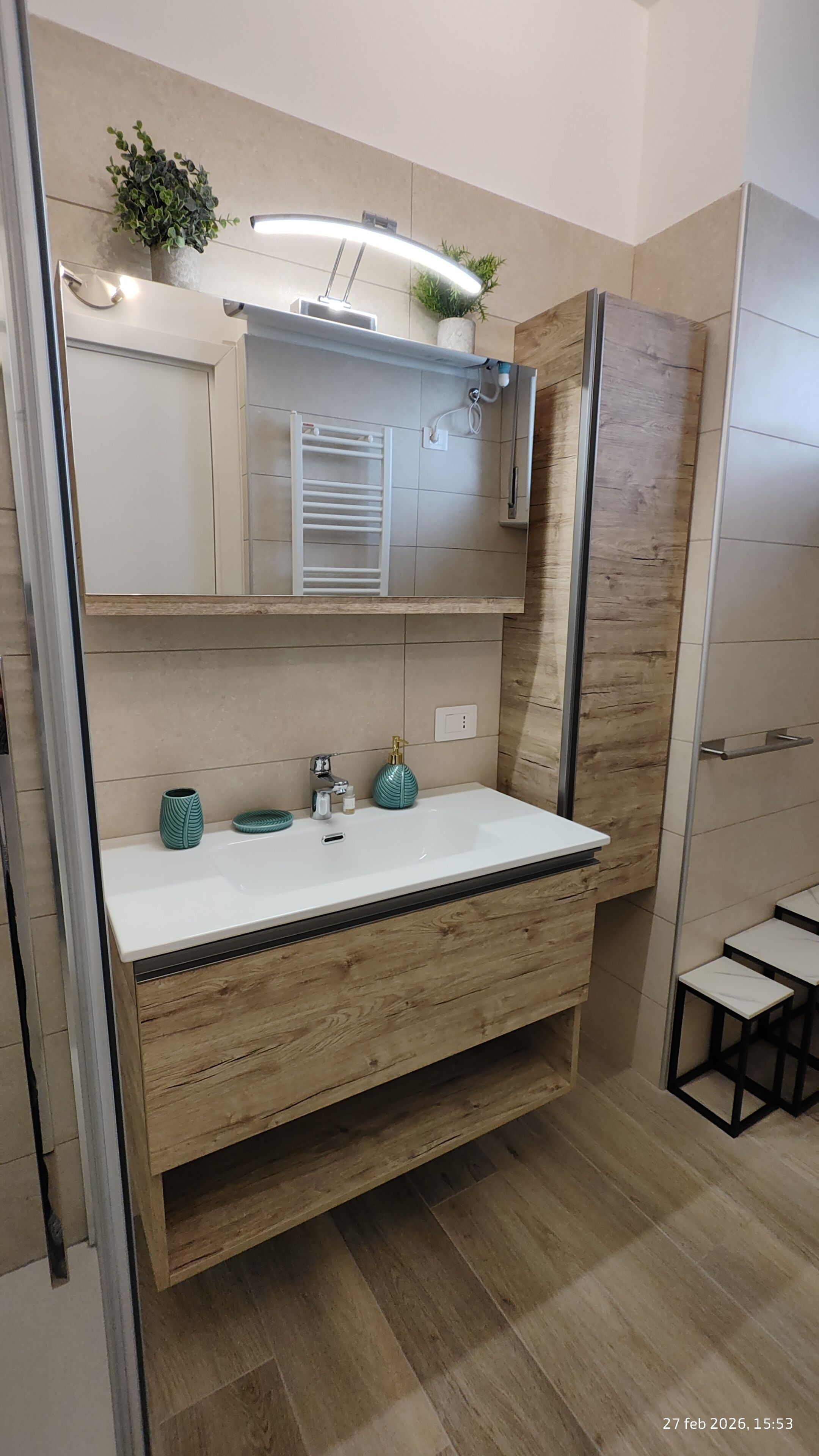 A modern bathroom with a wooden vanity, a white sink, and a mirror above it.