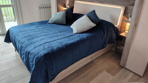 Ein modernes Schlafzimmer mit einem großen Bett, einem Holzkopfteil und Blick ins Freie durch eine Schiebetür.