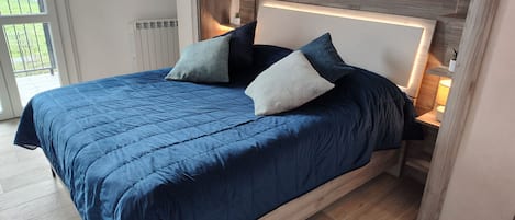Ein modernes Schlafzimmer mit einem großen Bett, einem Holzkopfteil und Blick ins Freie durch eine Schiebetür.