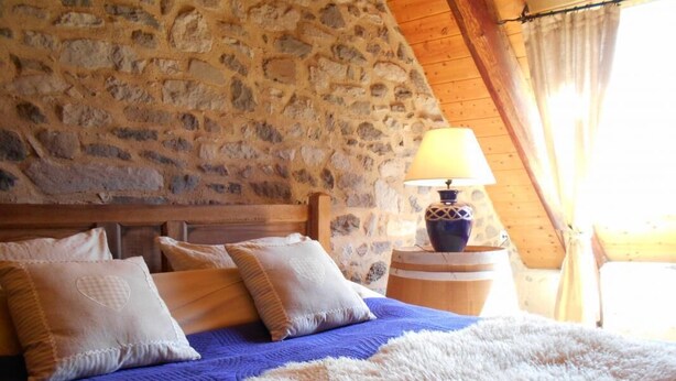 A bedroom with a stone wall, wooden ceiling, and a bed with blue bedding and white pillows. - Gîte de Brion en Cézallier (COMPAINS)