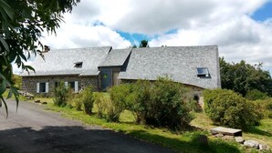A stone house with a sloped roof, a small garden, and a paved driveway. - Gîte de Brion en Cézallier (COMPAINS)