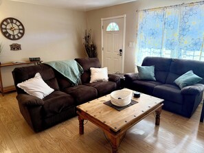 A living room with two sofas, a wooden coffee table, a clock, a welcome sign, and a door with a window. - Payson Getaway : Cozy 2-Bedroom Retreat (Payson)