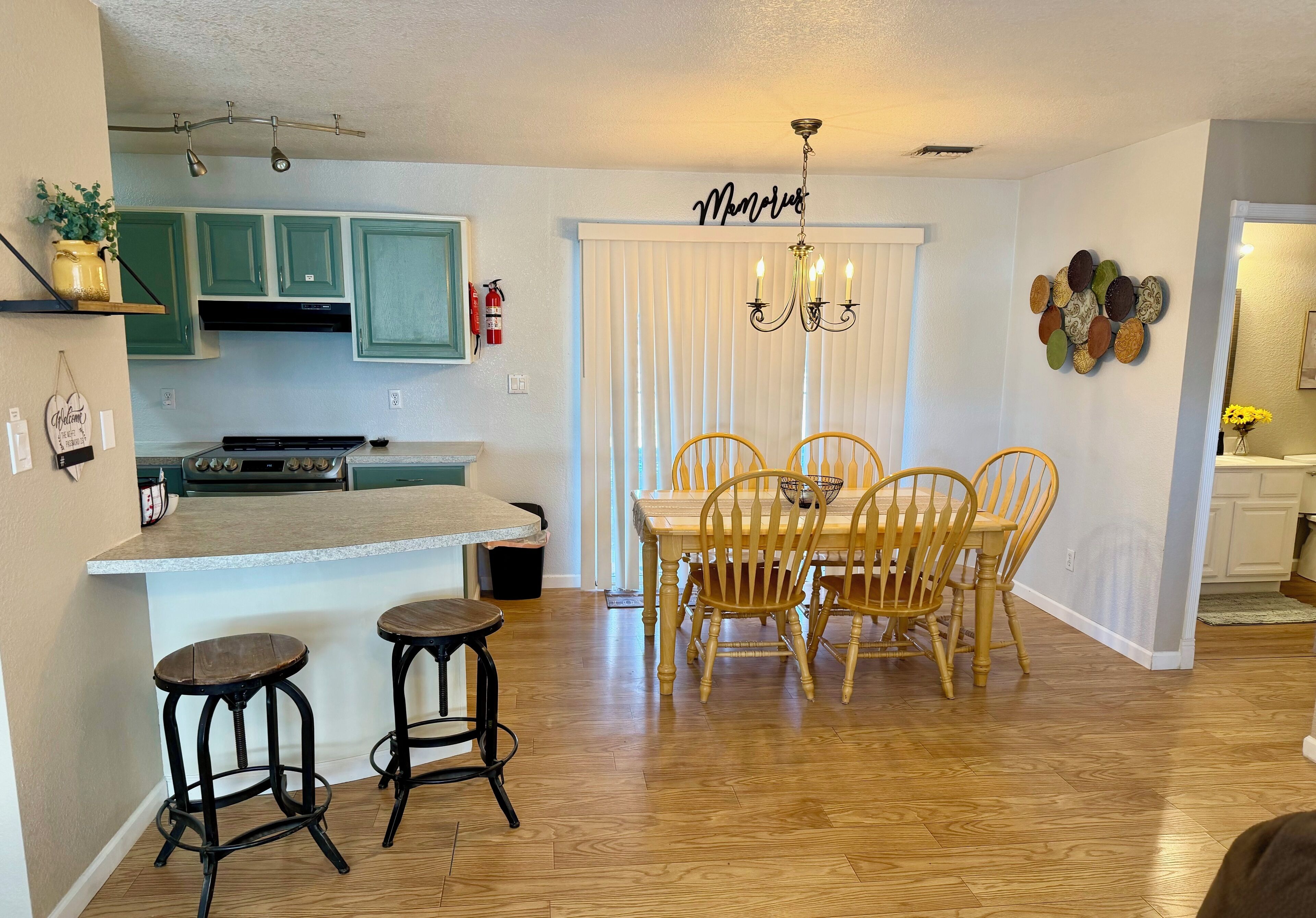 A kitchen with green cabinets, a central island with stools, a dining table with chairs, and a chandelier.