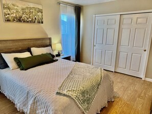 A neatly made bed with a patterned bedspread and pillows, a bedside lamp, a clock, and a window with curtains. - Payson Getaway : Cozy 2-Bedroom Retreat (Payson)