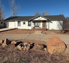 A single-story house with a prominent star on the front wall, a front porch with a bench, and a driveway leading to a garage. - Payson Getaway : Cozy 2-Bedroom Retreat (Payson)