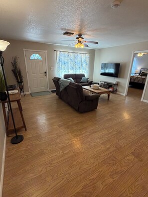 A spacious living room with a ceiling fan, a sofa, a coffee table, and a TV. - Payson Getaway : Cozy 2-Bedroom Retreat (Payson)