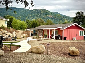 A red building with a covered patio, outdoor seating, and a gravel driveway. - Blossom Creek Retreat West A (Three Rivers)