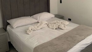 Ein ordentlich bezogenes Bett mit grauem Kopfteil, weißen Kissen und einer beigen Decke.
