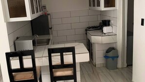Eine kleine Küche mit weißen Schränken, einer weißen Arbeitsplatte, einem Spülbecken, einem Herd, einem Toaster und zwei Stühlen.