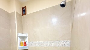 Ducha con azulejos color beige, repisa blanca con artículos de aseo y ducha.