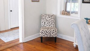 Una habitación con un sillón estampado, una ventana con frascos decorativos y una puerta que conduce a otra estancia.