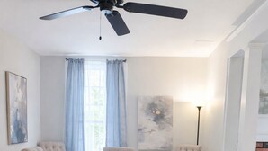 Un comedor con una mesa redonda, cuatro sillas tapizadas, un ventilador de techo y una alfombra sobre piso de madera.