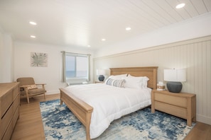 A bedroom with a wooden bed, a chair, a nightstand, a lamp, and a window with curtains.