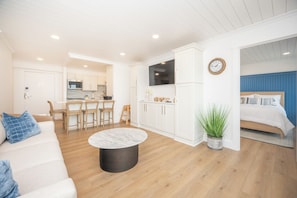 A modern living room with a sofa, a coffee table, a kitchen area with a TV, and a bedroom with a bed.