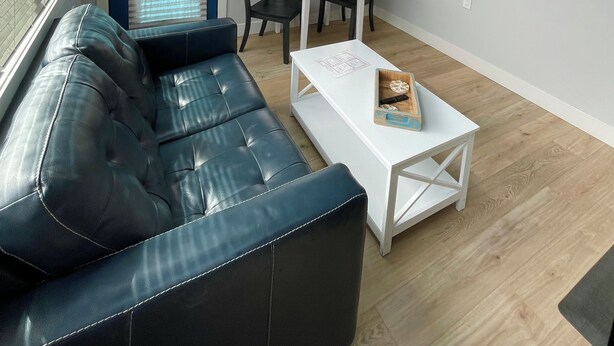 A modern living room with a black leather sofa, a white coffee table, and a dining area with a blue table and two chairs.