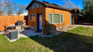 A single-story wooden house with a patio, a barbecue grill, and a small garden area.