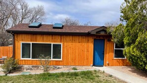 A wooden house with a blue door, large windows, and solar panels on the roof.