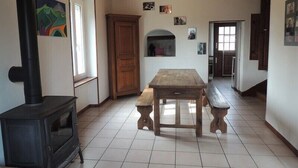 Una habitación con una mesa de madera, bancos, una estufa y una puerta que da a otra habitación.