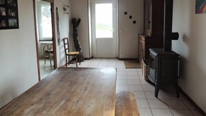 Una habitación con piso de madera, una puerta que da a otra estancia, una silla, un mueble pequeño y un calefactor negro.