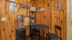 A wooden interior with a fireplace, a table, two chairs, and various signs including one that says 'this is our place.' - Cozy, Modern Black Cabin Retreat - Mins. to Cloudland Canyon & Lookout Mountain (Rising Fawn)
