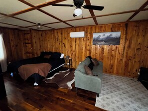 Una habitación con paredes de madera, una cama, una silla, un ventilador de techo y un cuadro en la pared.
